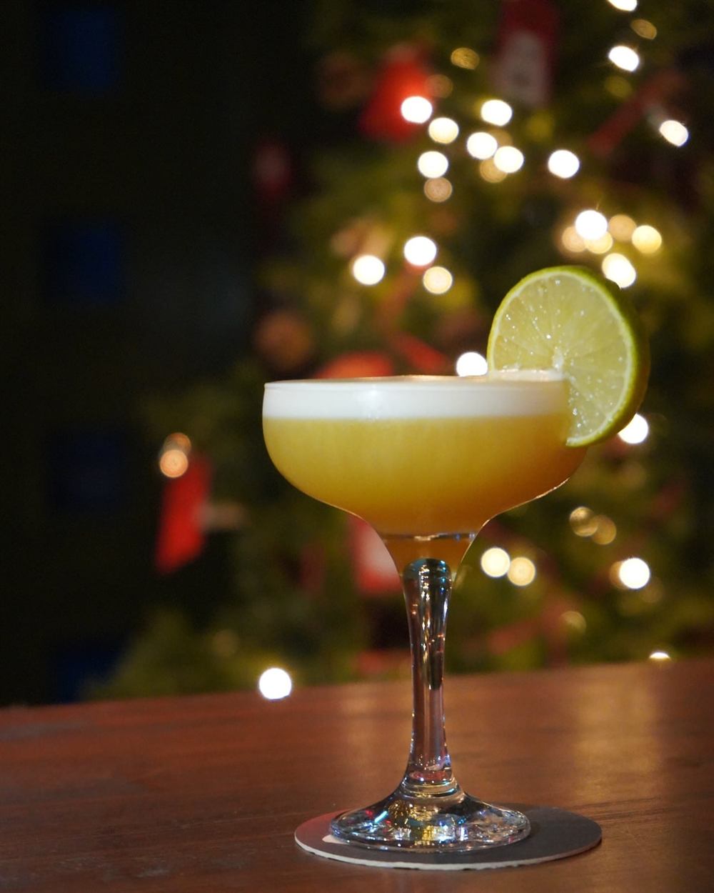 A whiskey sour in a coupe glass with a lime wheel, fairy lights glowing behind.