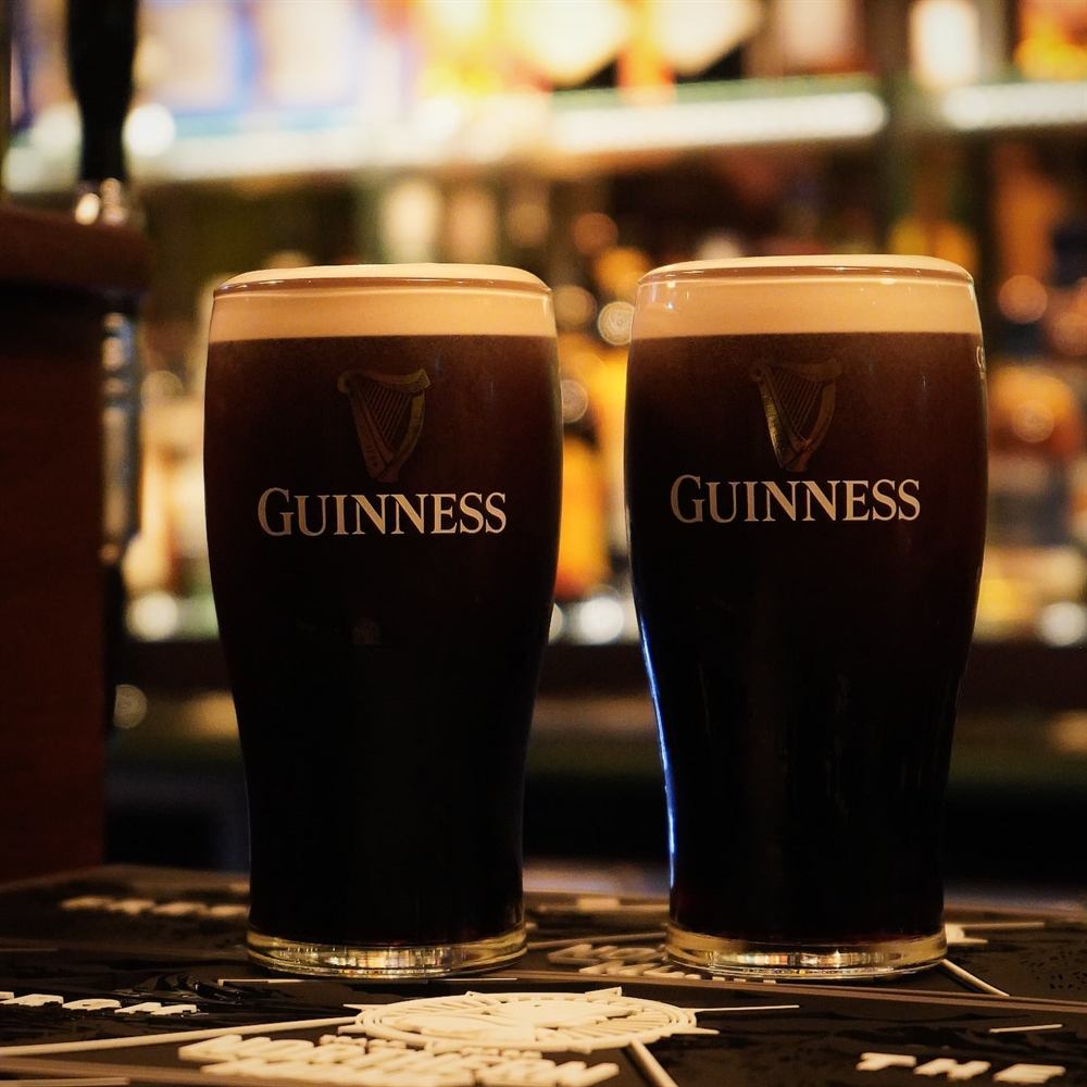 Two pints of Guinness settling on the bar in front of the spirits shelf.